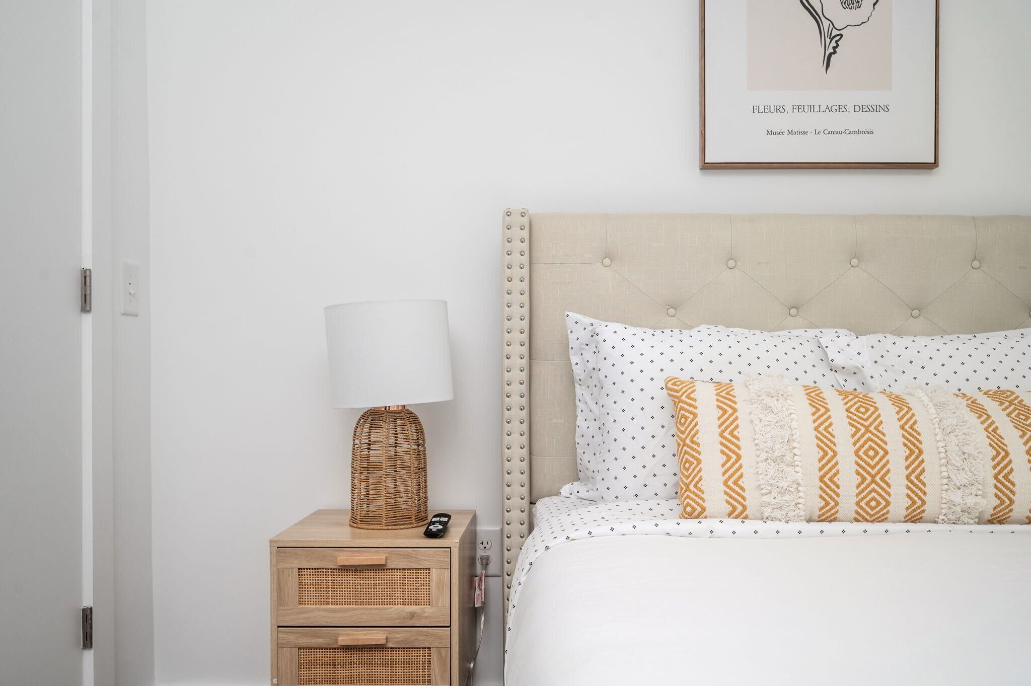 A bedroom with a bed, a nightstand with a lamp, and a framed artwork on the wall.