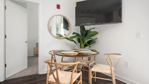A dining area with a round table, four chairs, a mirror, a potted plant, and a mounted TV.