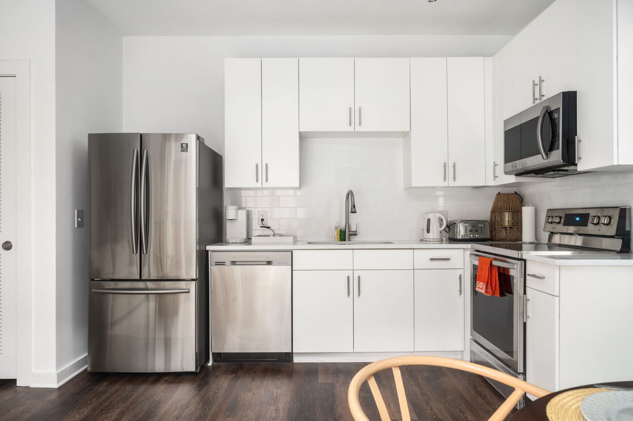 A modern kitchen with white cabinets, stainless steel appliances, and a wooden dining table.