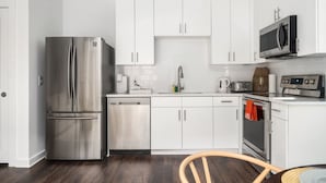 A modern kitchen with white cabinets, stainless steel appliances, and a wooden dining table.