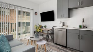 A modern kitchen with grey cabinets, a flat-screen TV, and a dining area with a table and chairs. - Upgraded Apartment in Old Fourth Ward (Atlanta)