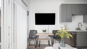 A modern kitchen with grey cabinets, a flat-screen TV, a dining table with chairs, and a small potted plant. - Upgraded Apartment in Old Fourth Ward (Atlanta)