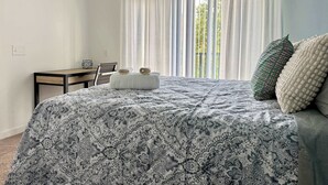 A bedroom with a bed, a desk, and a chair. There is a window with curtains.