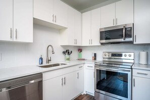 A modern kitchen with white cabinets, stainless steel appliances, a dishwasher, and a microwave.