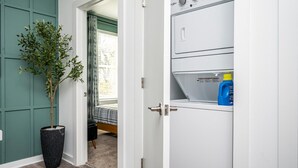 Ett tvättrum med en tvättmaskin, en krukväxt och en säng i bakgrunden.