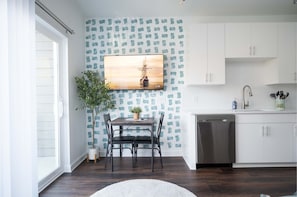 A modern kitchen with white cabinets, a dishwasher, and a dining area with a table and chairs.