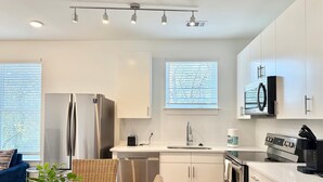 A modern kitchen with white cabinetry, stainless steel appliances, and a dining area with a wooden table and wicker chairs. - Downtown 1B1B Modern Apartment! Free Street Parking! (Atlanta)