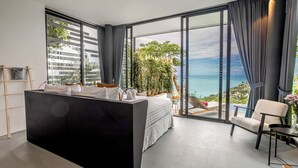 A modern hotel room with a large bed, a small desk, a chair, and a view of the ocean. - Hin Butik Villa 4BR Private Seaview (Koh Samui)