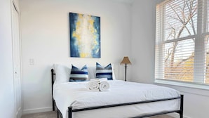 A bedroom with a bed, white bedding, and a blue abstract painting on the wall.