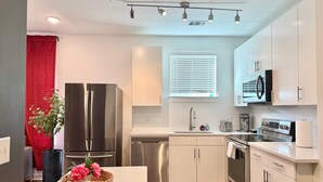 A modern kitchen with stainless steel appliances, a white countertop, and a dining area with a black chair and a woven basket with flowers.