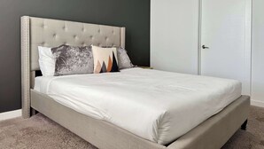 Ein Bett mit einer gesteppten Kopfteil, einer neutralen Matratze und einigen Kissen.