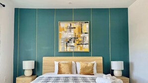 Una habitación de hotel con una cama grande, dos mesitas de noche con lámparas, una pared verde de acento y un cuadro abstracto enmarcado.