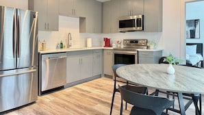 Una cocina moderna con electrodomésticos de acero inoxidable, armarios grises y una mesa de comedor redonda.