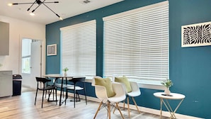 Una sala de estar moderna con una pared azul de acento, un comedor con sillas negras y blancas, y una cocina visible a través de un umbral abierto.