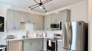 A modern kitchen with stainless steel appliances, grey cabinets, and a wooden floor. - Modern Multi-level 2B2B Apartment in Old Fourth Ward (Atlanta)