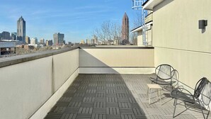 A rooftop terrace with a patterned floor, two metal chairs, and a view of a city skyline. - Modern Multi-level 2B2B Apartment in Old Fourth Ward (Atlanta)