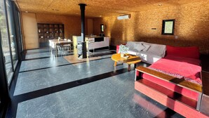 Ein modernes Interieur mit Holzbalkendecke, einem zentralen Kamin, einer Couch und einem Essbereich.