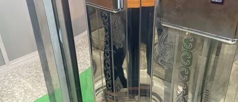 Un ascensor con paredes metálicas reflectantes y piso cubierto de moqueta verde.