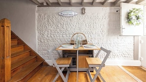 A wooden staircase leading to a dining area with a textured white wall, a 'Welcome to Beach House' sign, and a door with a wreath. - Cosy Character Cottage by the Sea (East Wittering)