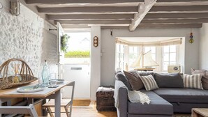 A cozy living room with a gray sofa, wooden dining table, and a window with a sailboat decoration. - Cosy Character Cottage by the Sea (East Wittering)