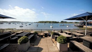 A waterfront patio with wooden benches and tables, overlooking a calm lake with several boats.