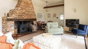 A cozy living room with a brick fireplace, striped armchairs, a television, and a sofa.