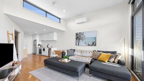A modern living room with a grey sofa, a flat-screen TV, and a dining area with a wooden table. - Inlet Apartment I Walk to beach, cafes and more (Aireys Inlet)