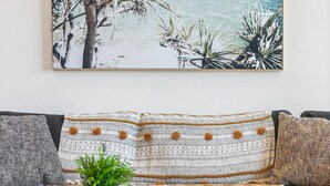 A living room with a grey sofa, a patterned throw pillow, a small wooden tray with a plant, and a framed picture of a beach scene. - Inlet Apartment I Walk to beach, cafes and more (Aireys Inlet)
