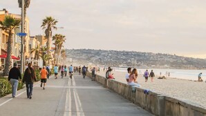 A coastal promenade with a concrete walkway, palm trees, and a beach in the background. - Boho Bliss | Mission Beach Retreat w/ Surfboards (San Diego)