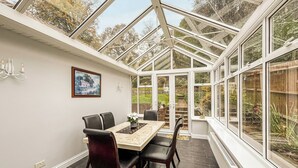 A conservatory with a dining table, chairs, and a view of the garden.