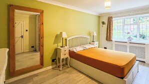 A bedroom with a bed, bedside tables, a mirror, a window with curtains, and a ceiling light fixture.
