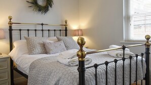 Een net opgemaakt bed met een gewatteerde spreideken, een decoratieve krans aan de muur en een raam met jaloezieën.