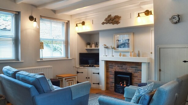 Een woonkamer met een open haard, twee blauwe banken, een televisie en een klok aan de muur.
