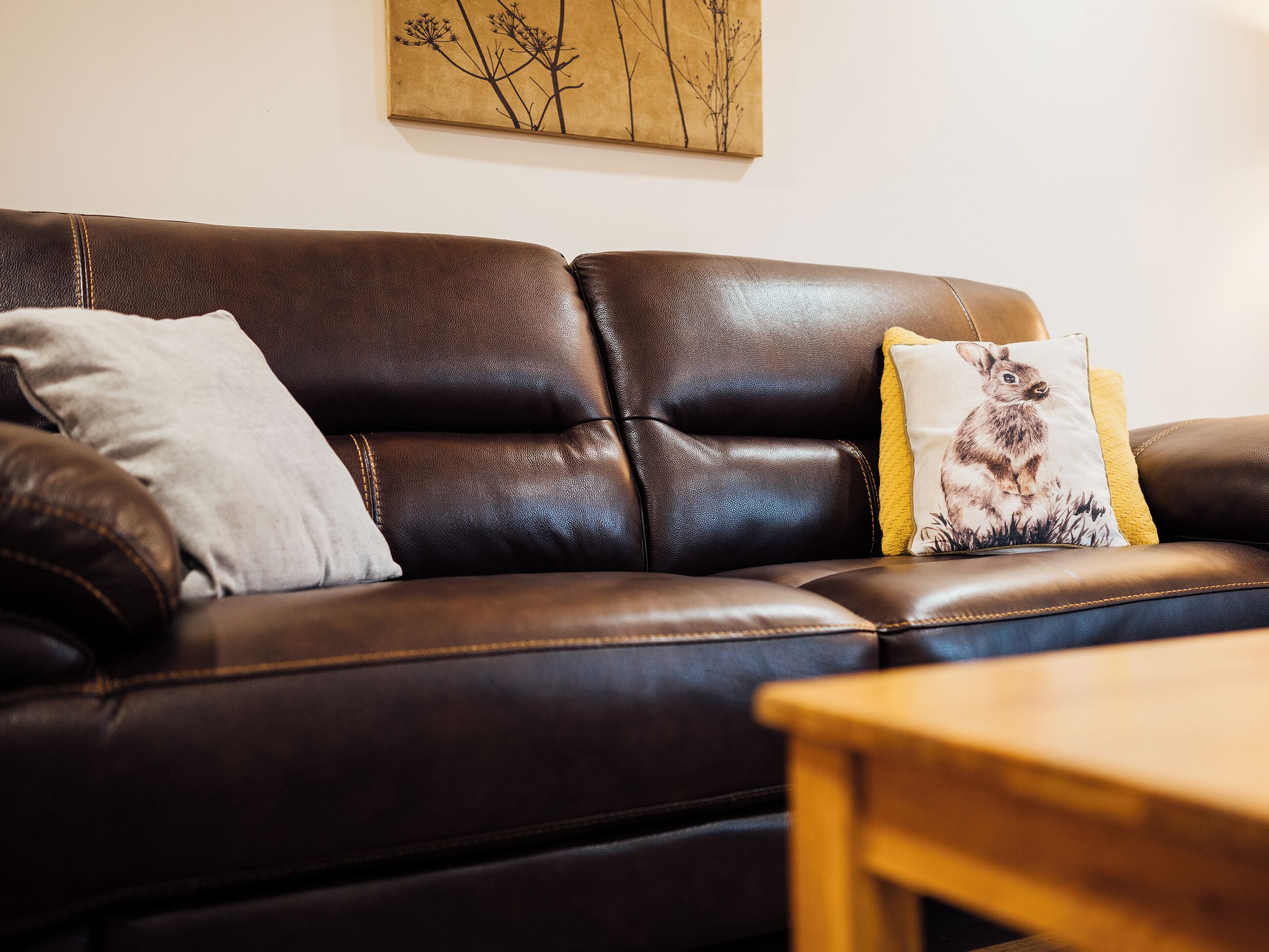 A brown leather sofa with two cushions, a wooden coffee table, and a wall art piece.