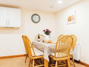 Un coin repas avec une table dressée pour deux personnes, une horloge au mur et un tableau encadré représentant un renard.