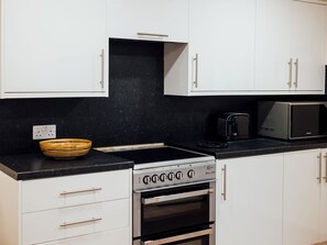Une cuisine avec des armoires blanches, un plan de travail noir, une cuisinière, un four et un four à micro-ondes.