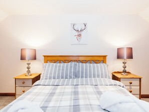 A bedroom with a wooden headboard, a plaid bedspread, two bedside tables with lamps, and a wall-mounted deer artwork.