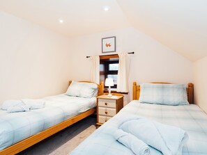 A bedroom with two beds, a nightstand, a window with curtains, and a picture on the wall.
