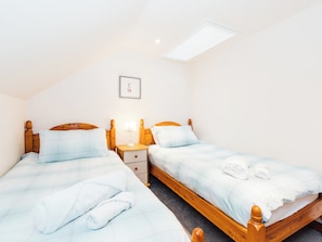Een slaapkamer met twee houten bedden, een nachtkastje, een kleine tafel, een lijst met een afbeelding en een dakraam.
