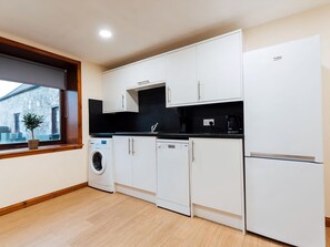 Une cuisine moderne avec des meubles blancs, un plan de travail noir, un lave-linge, un lave-vaisselle et un réfrigérateur.