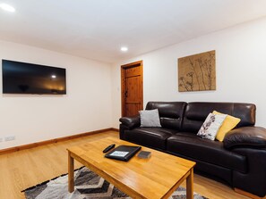 Un salon avec une table basse en bois, un canapé en cuir, un téléviseur à écran plat et une porte en bois.