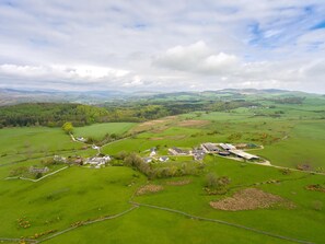 Un paysage rural avec un vaste domaine comprenant plusieurs bâtiments, de vastes champs et une chaîne de montagnes à l’horizon.