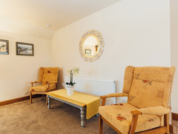 A room with two armchairs, a small table, a mirror, and two framed pictures on the wall.