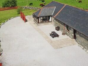 A stone building with a sloped roof, a covered outdoor seating area, and a gravel driveway.
