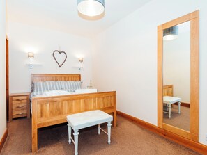 Quarto com cama de madeira, mesas de cabeceira, um banco, um espelho grande e luminárias fixadas na parede.