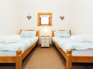 A twin room with two wooden beds, a nightstand, a window with a wooden frame, and heart-shaped wall decorations.