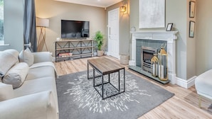 Una sala de estar con sofá, mesa de centro, televisor, chimenea y lámpara.