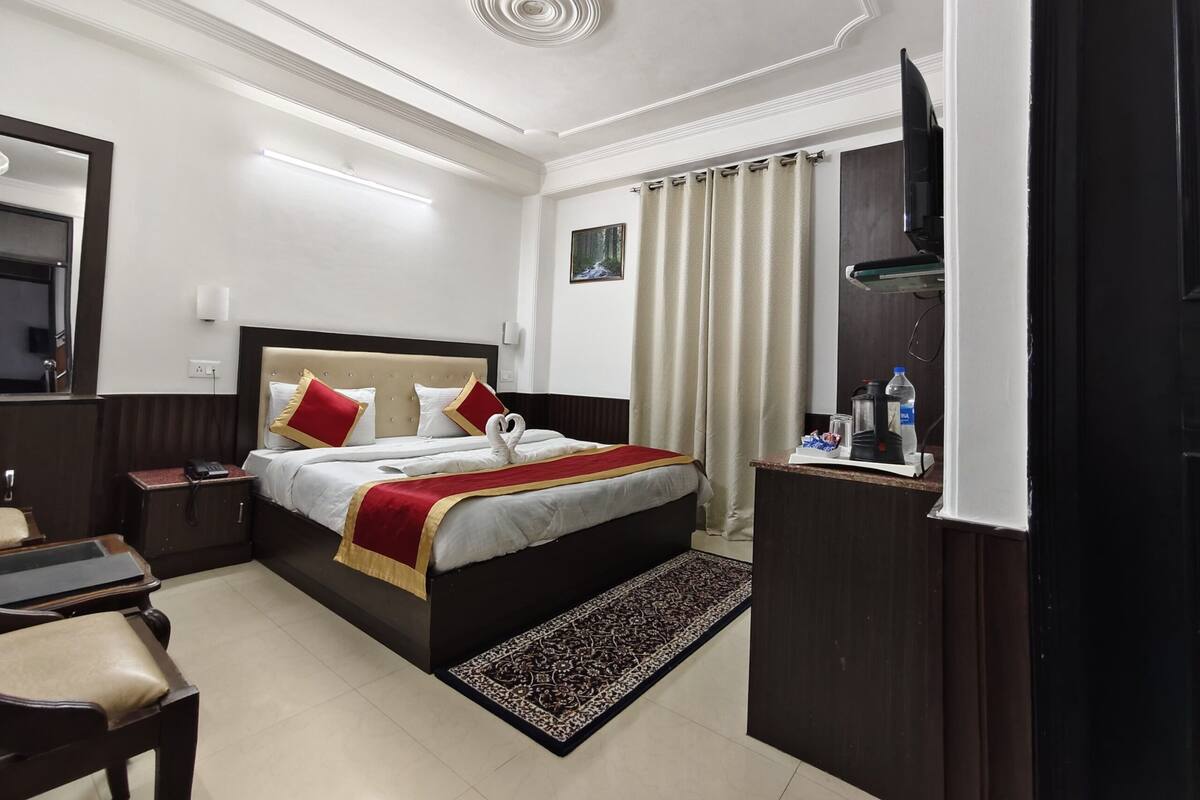 A hotel room with a bed, bedside table, TV, and a small desk with a chair.