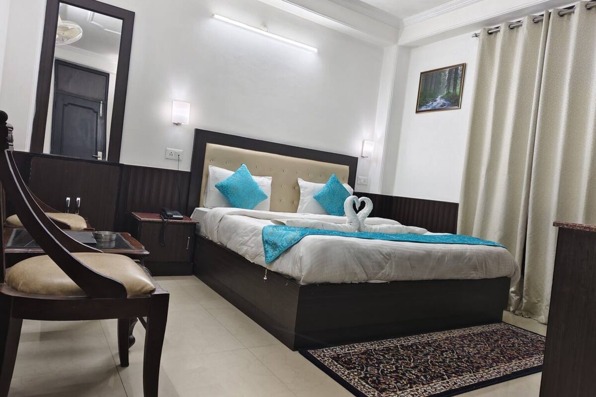 A hotel room with a large bed, a chair, a nightstand, a mirror, and a painting on the wall.
