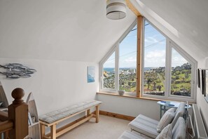 A room with a large window, a bench, a table, and a bed.